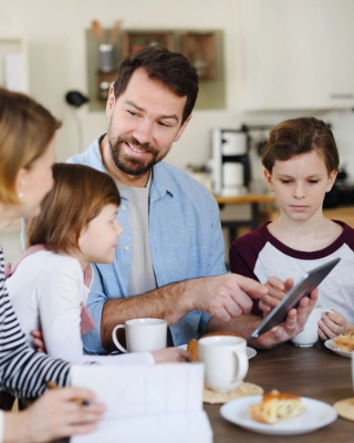 Eine Mutter und ein Vater sind mit ihren beiden Kindern am Frühstücken und diskutieren gemeinsam über das Taschengeld.